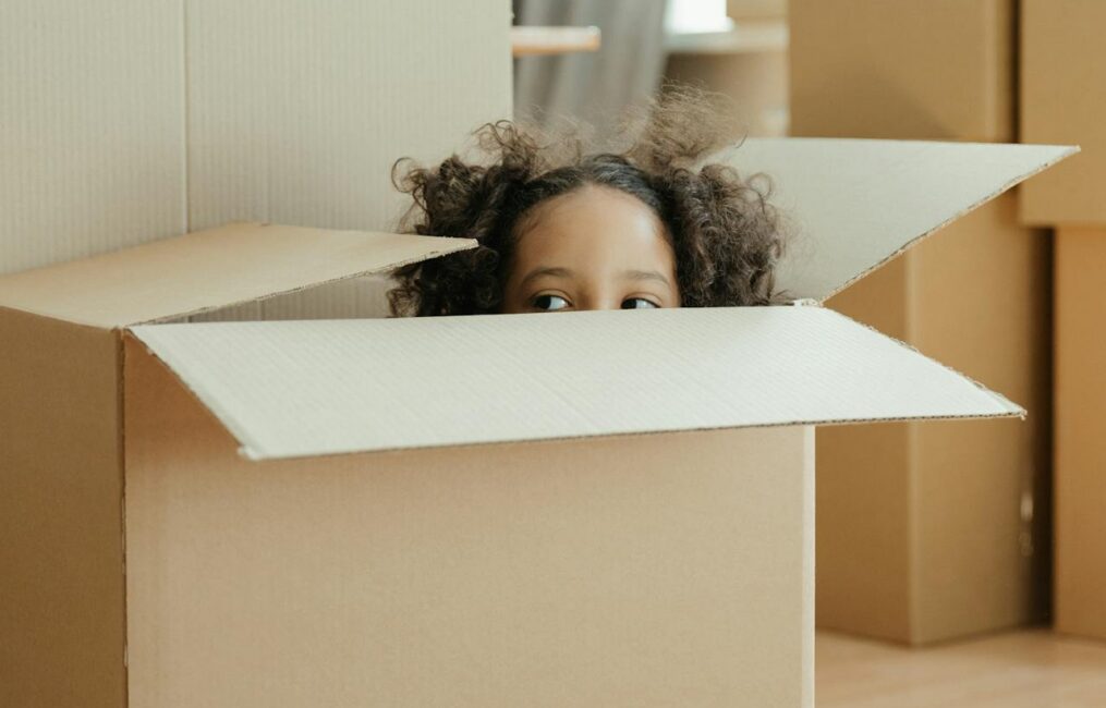 Child playing inside a cardboard moving box during a family move