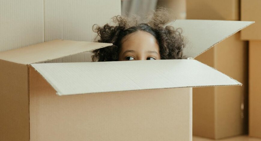 Child playing inside a cardboard moving box during a family move
