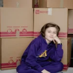 Child sitting beside packed moving boxes during a family home move