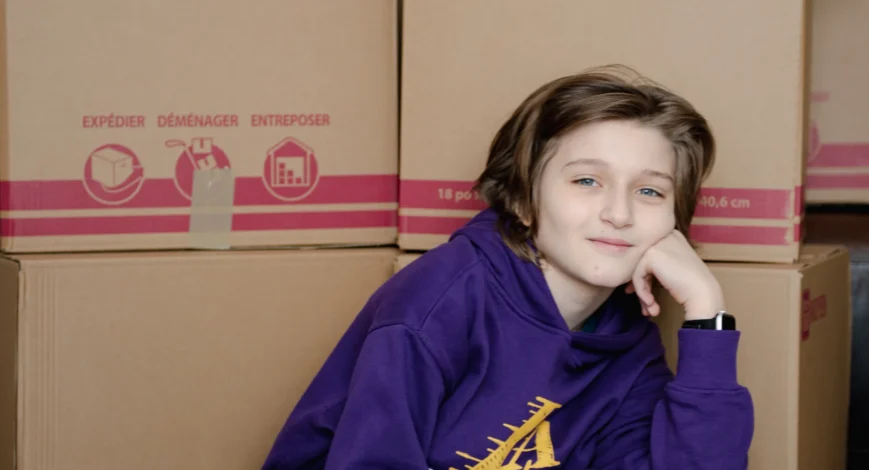 Child sitting beside packed moving boxes during a family home move